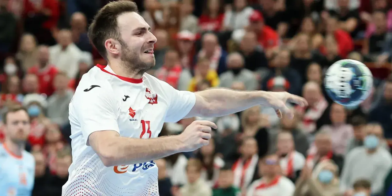 Piłkarz ręczny Polski w akcji, rzuca piłkę. W tle widać trybuny z kibicami, którzy dopingują swoją drużynę w meczu przeciwko Iranowi.