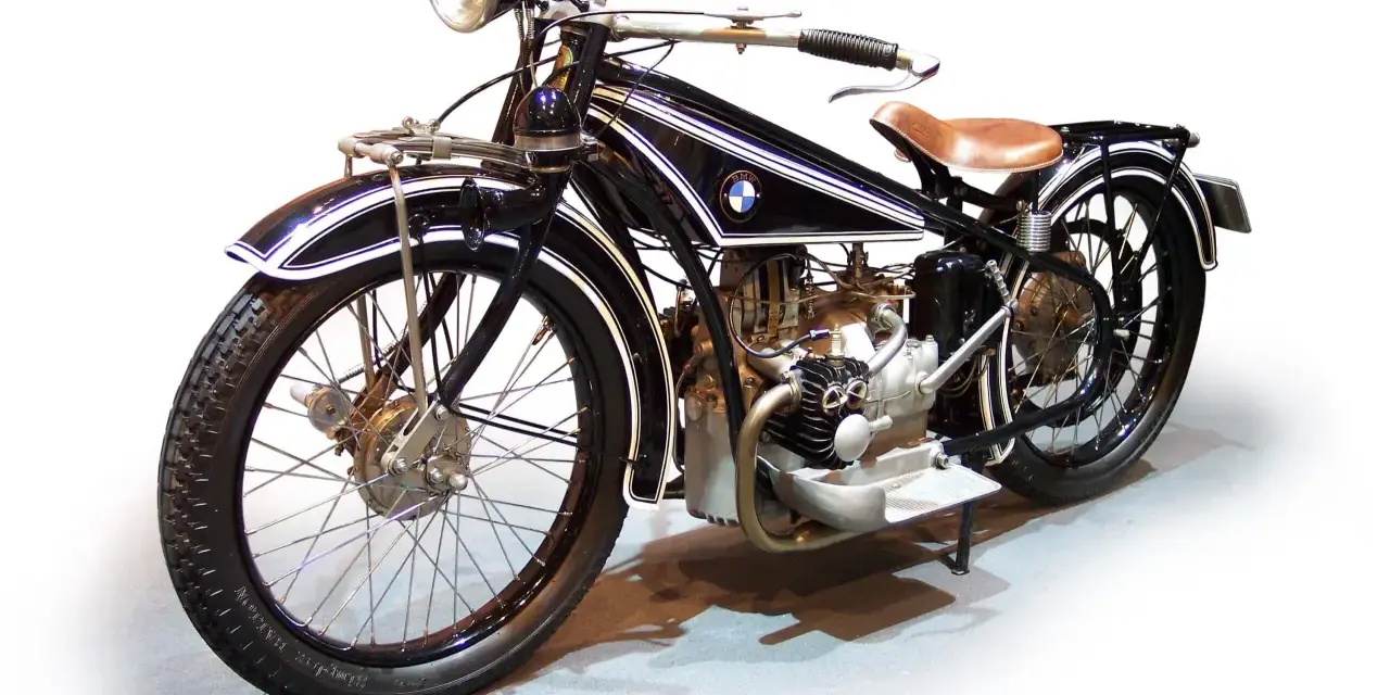 Klasyczny motocykl BMW z lat 20. XX wieku, czarny z białymi pasami, z brązowym siodłem. Ikona historii BMW.