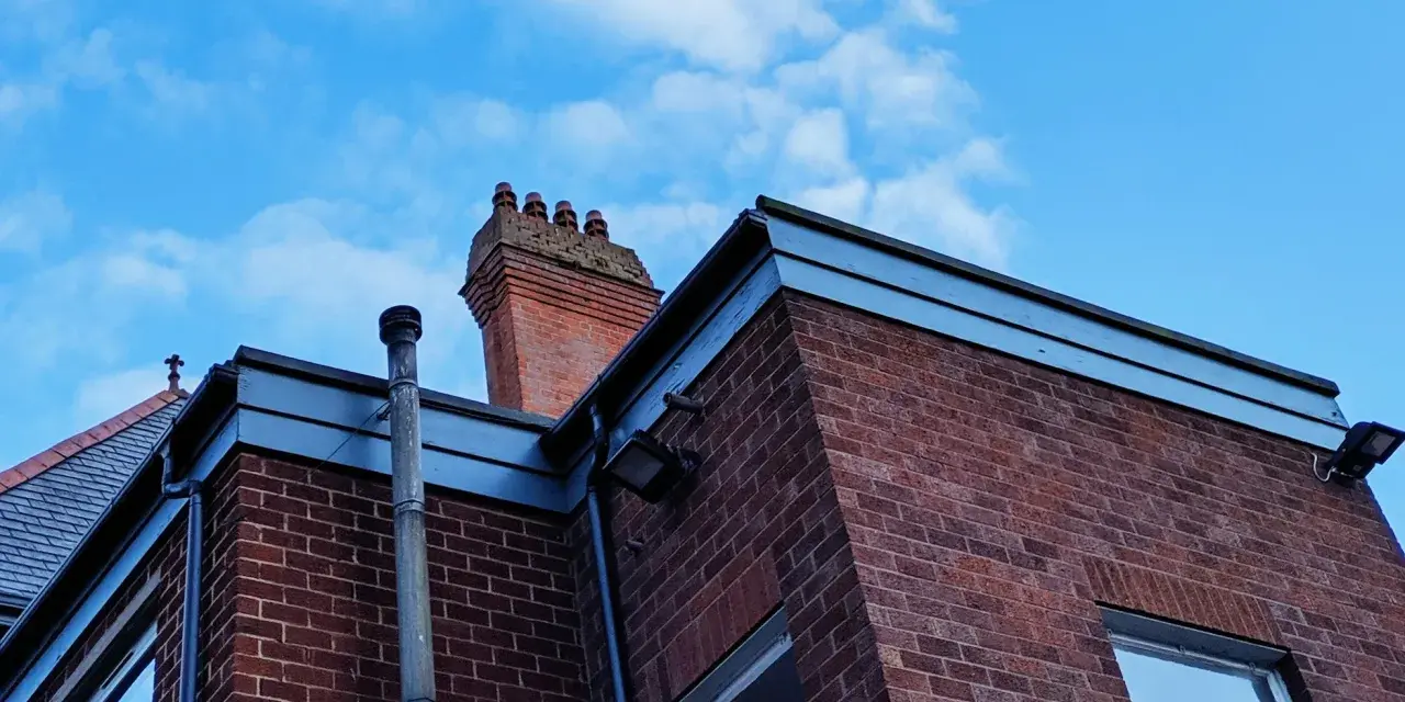 Vue d'une maison en briques rouges avec une cheminée traditionnelle et un conduit de poêle à bois sortie ventouse en façade. Ciel bleu avec quelques nuages.