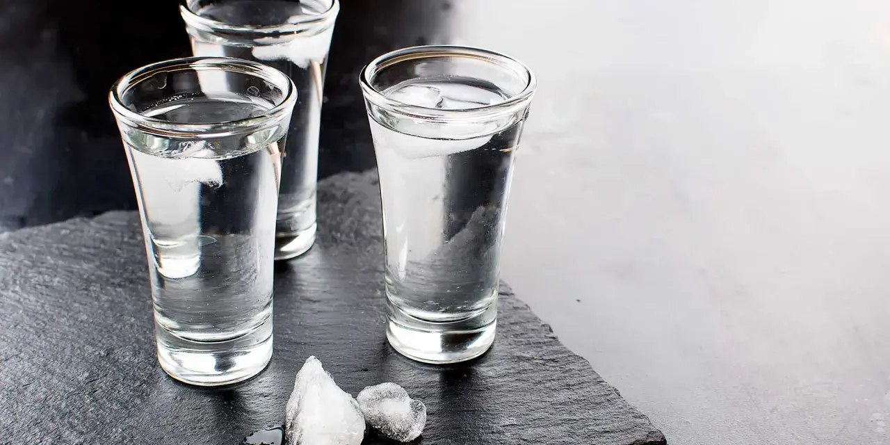Drei Gläser Wodka mit Eiswürfeln auf dunklem Stein. Wodka wird aus Getreide oder Kartoffeln hergestellt.