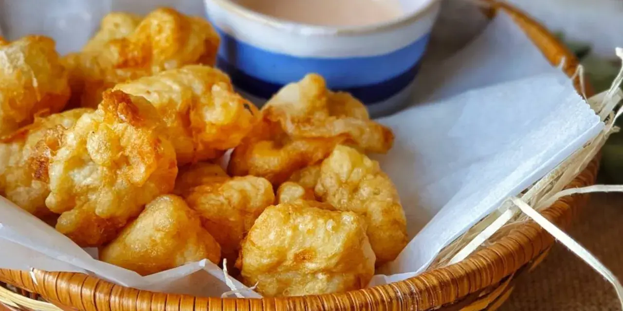 Cesta de mimbre con crujientes fritos de pixin, acompañados de una cremosa salsa rosa. ¡Un bocado delicioso!