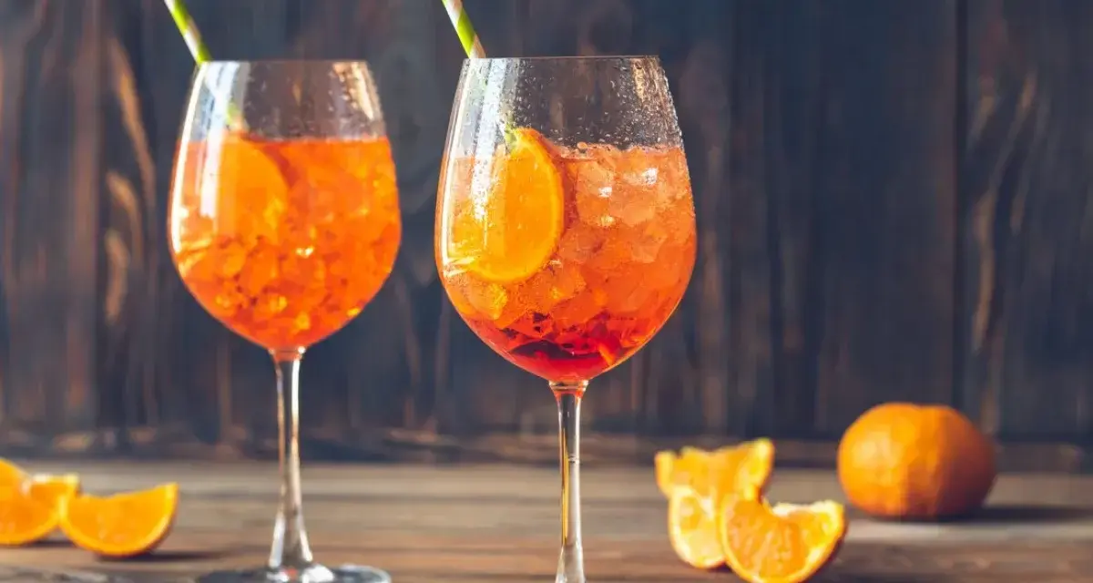 Dwa orzeźwiające drinki z sokiem pomarańczowym, lodem i plasterkiem pomarańczy, ozdobione słomkami.