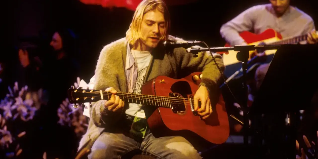 Kurt Cobain gra na gitarze akustycznej, czuć atmosferę, która pachnie nirvaną.