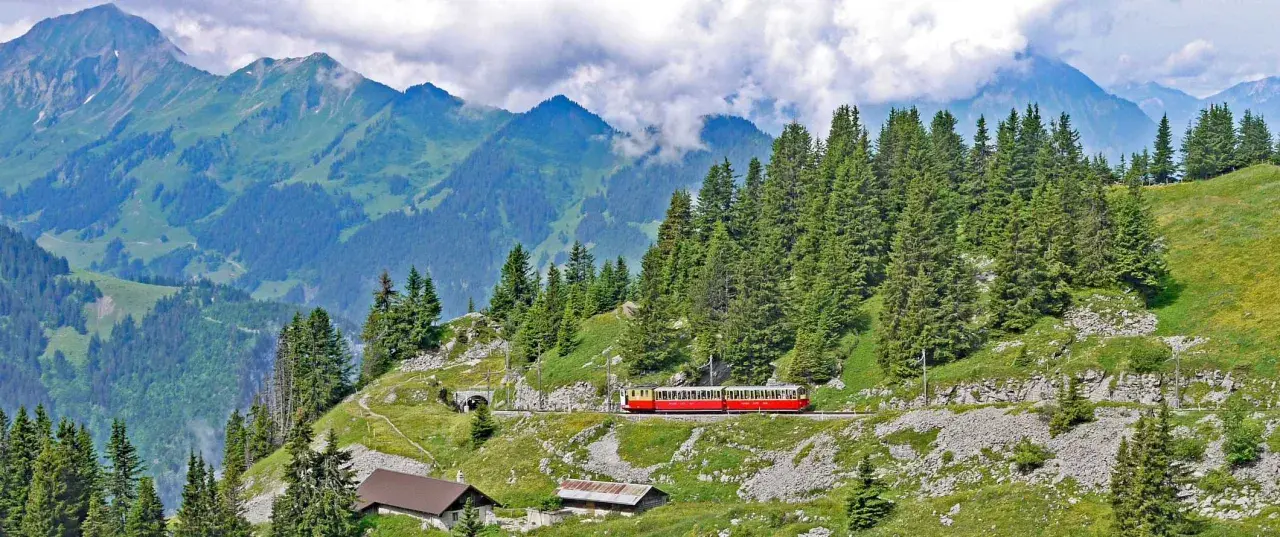 A red and yellow cogwheel train winds through the Swiss Alps, a scenic way to get around Interlaken.