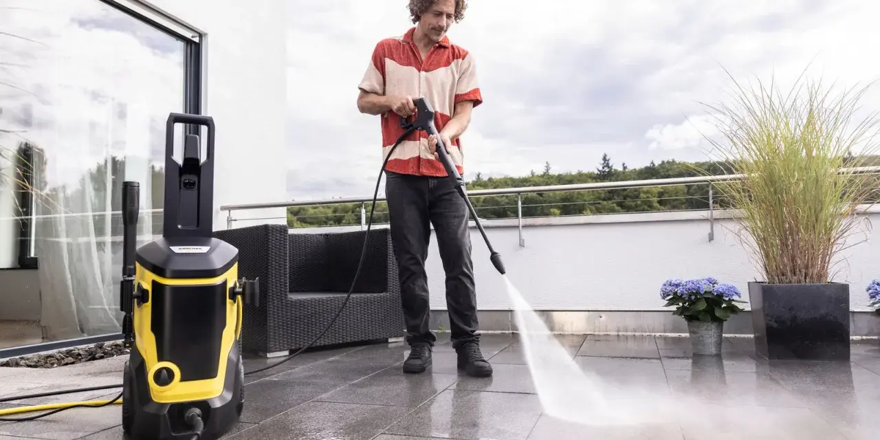 Man rengör altanen med en Kärcher K7. Tillbehör som högtryckstvätt och slang syns tydligt.