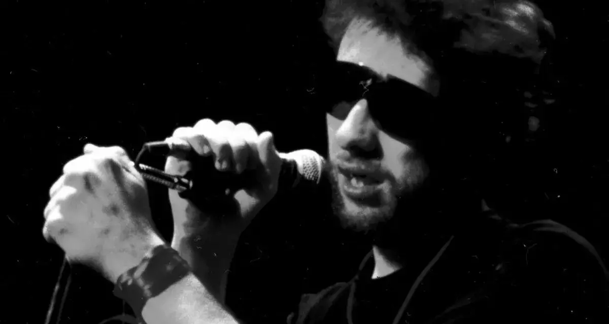 Chanteur d'un groupe irlandais punk, lunettes de soleil, micro en main, sur scène.