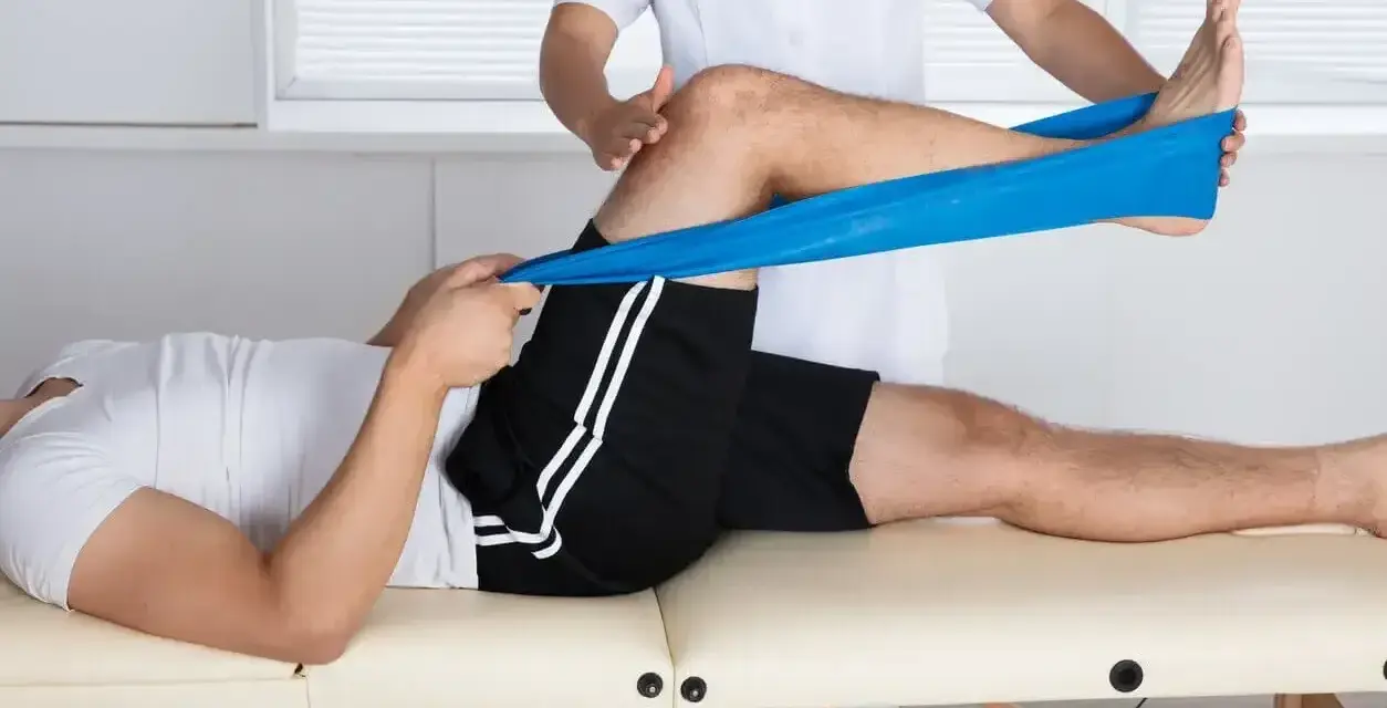 Therapeut dehnt Bein mit blauem Band zur Behandlung von Plica-Syndrom, inspiriert von Liebscher & Bracht Methoden.