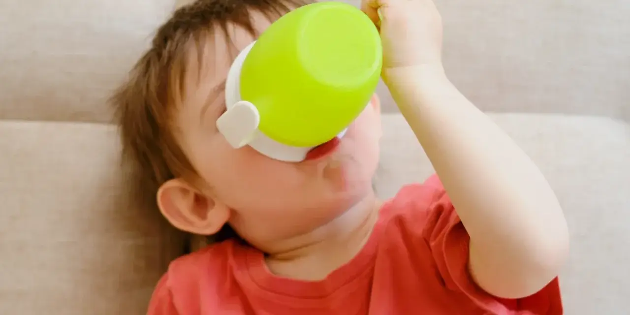 Małe dziecko pije z zielonego kubka niekapka LOVI.