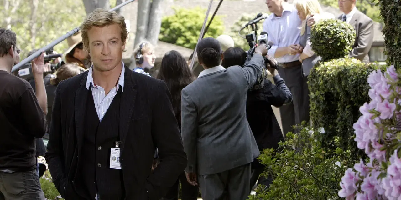 Simon Baker, con la sua nuova fidanzata, è circondato da telecamere e microfoni durante un evento all'aperto.
