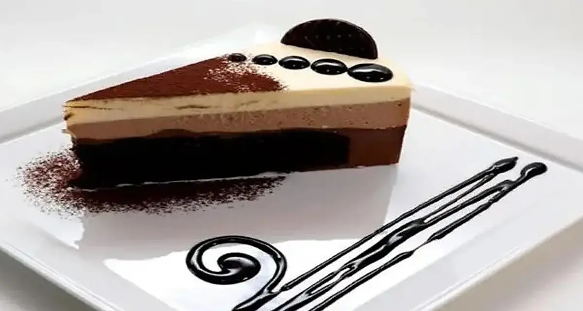 Una rebanada de tarta de tres chocolates, con capas de mousse de chocolate blanco, con leche y negro, espolvoreada con cacao y decorada con chocolate.