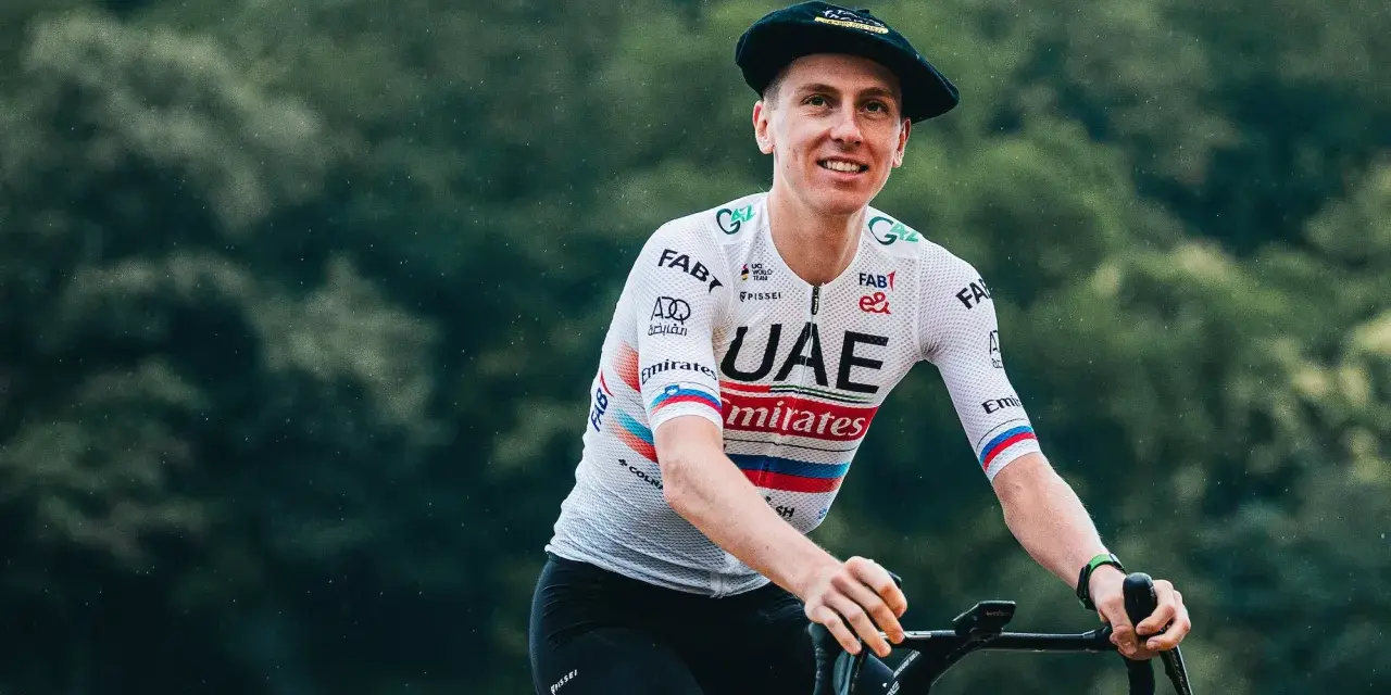 Tadej Pogačar, known for his incredible VO2 max, smiles while riding his bike in a UAE Emirates jersey and a Basque beret.