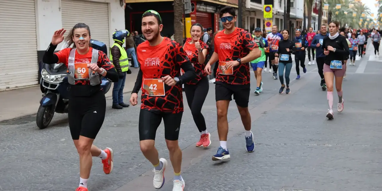 Corredores alegres participan en una media maratón, con dorsales visibles. El ambiente festivo sugiere un evento deportivo emocionante, parte de un calendario de medias maratones.