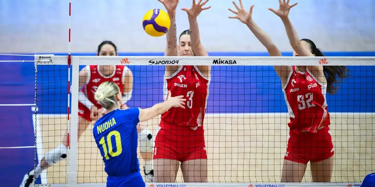 Piłka leci nad siatką podczas meczu liga światowa w piłce siatkowej. Zawodniczki w czerwonych strojach próbują ją zablokować.
