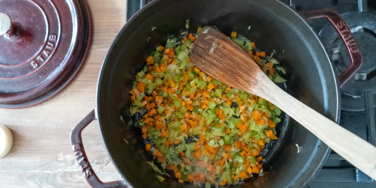 Würfel aus Karotten, Sellerie und Zwiebeln werden in einem Topf für ein soffritto rezept angedünstet.