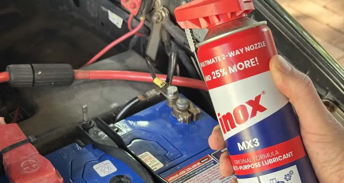 A hand holds a can of INOX MX3 lubricant near a car battery. Does cleaning battery terminals help? This spray might be the answer.