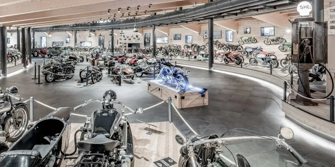 Wnętrze muzeum motocykli pełne zabytkowych maszyn, w tym motocykli z wózkami bocznymi i klasycznych samochodów.