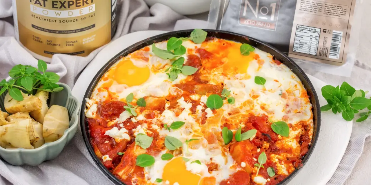 Pyszne śniadanie low carb: jajka sadzone w sosie pomidorowym z fetą i ziołami, obok pieczone karczochy. Obok produkty BE KETO.