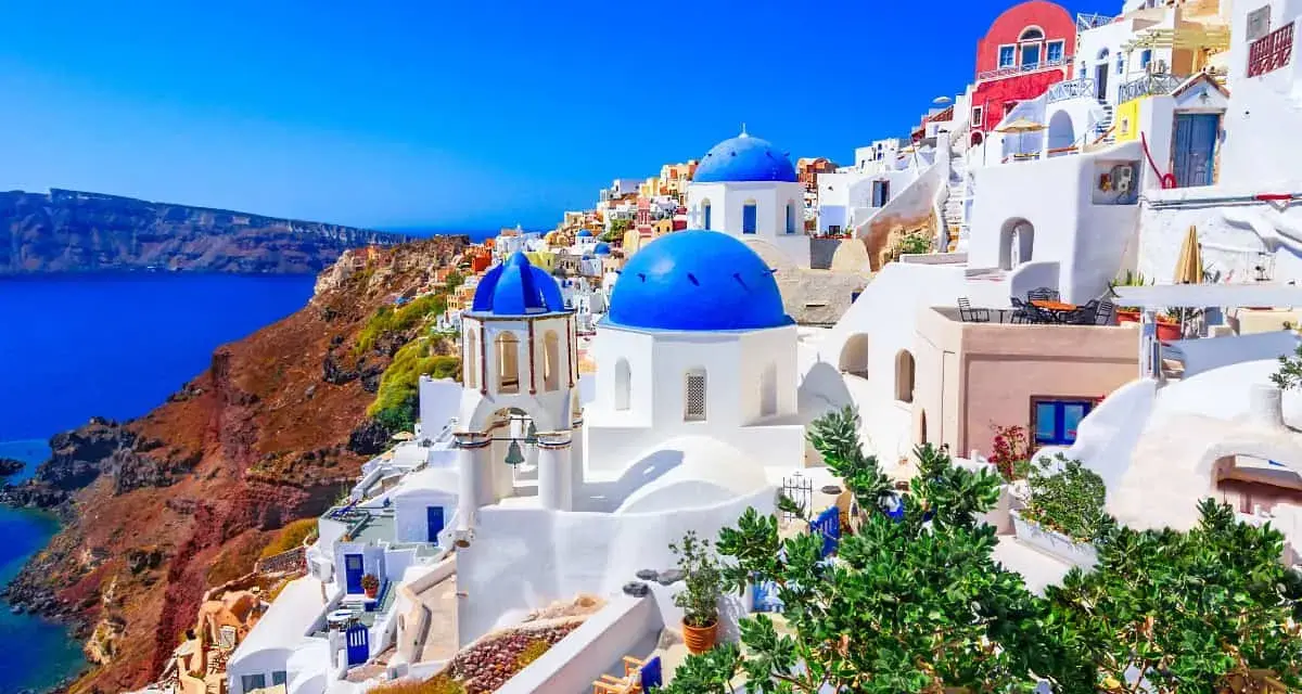 Santorini wakacje: białe domy z niebieskimi kopułami na zboczu klifu nad lazurowym morzem. Idealne miejsce na wymarzone wakacje.