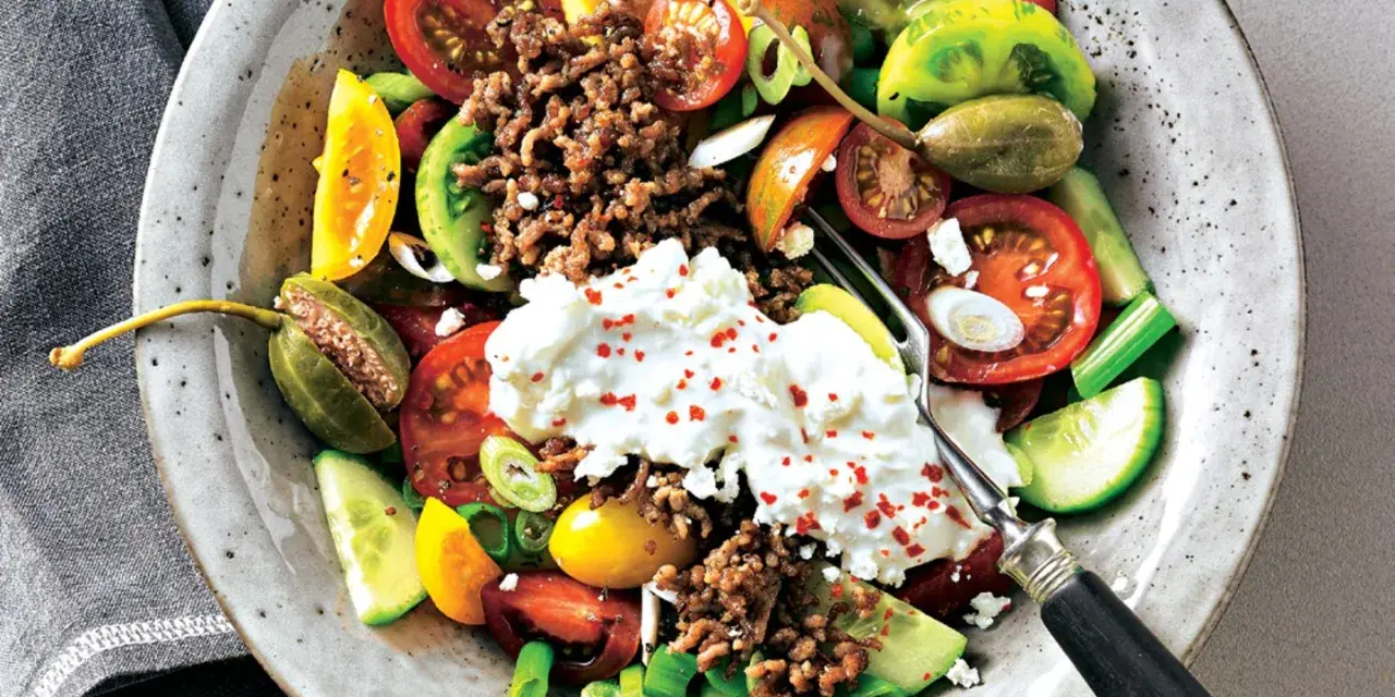 Bunter Tomatensalat mit Feta, Hackfleisch und Kapern. Frische Tomaten, Gurken und Frühlingszwiebeln bilden die Basis für diesen herzhaften Salat.
