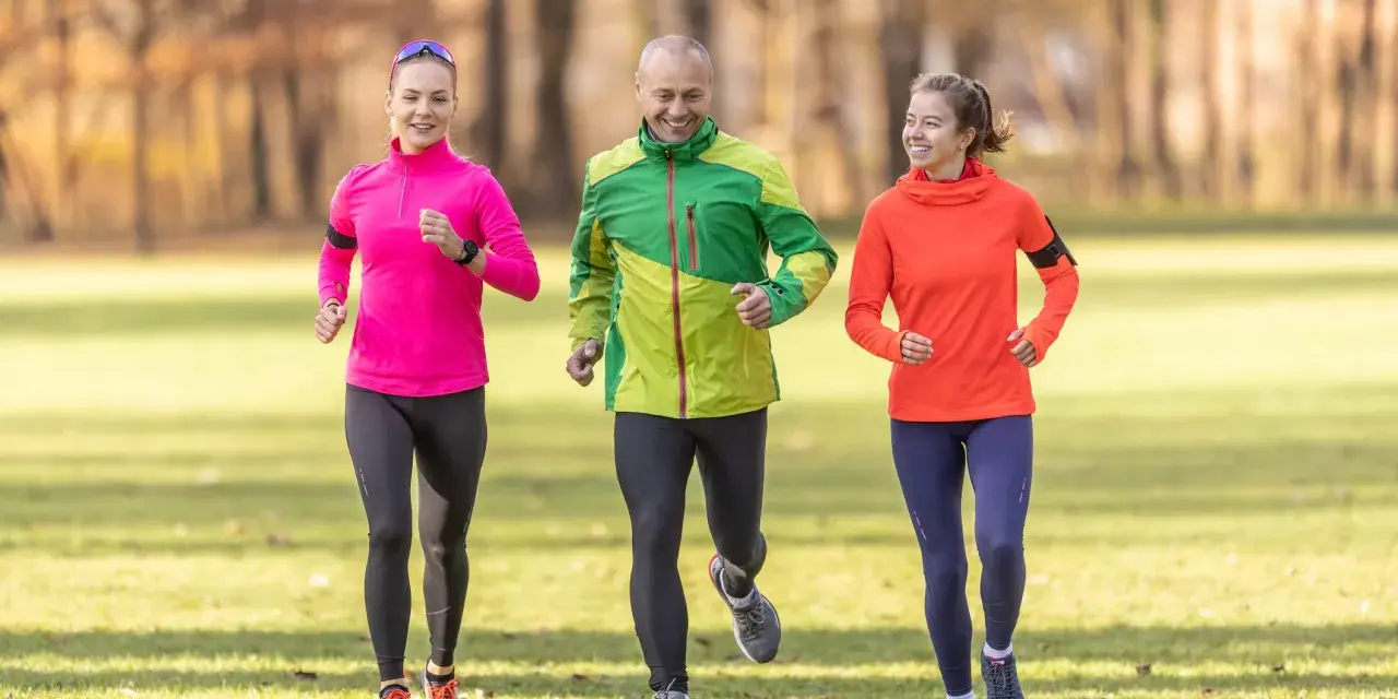 Un gruppo di amici sorridenti segue un programma allenamento corsa e camminata in un parco autunnale.