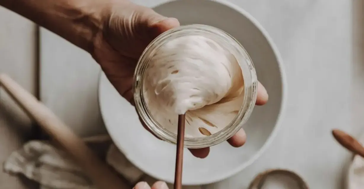 Eine Hand hält ein Glas mit lebendigem Sauerteig, bereit zum Auffrischen. Blasen und Luftlöcher zeigen seine Aktivität.