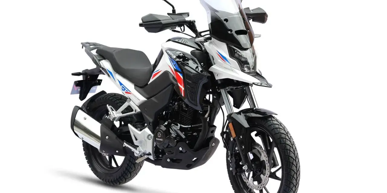 Nowy motocykl gotowy do docierania. Biało-czarny z czerwono-niebieskimi akcentami, z wysoką szybą i terenowymi oponami.