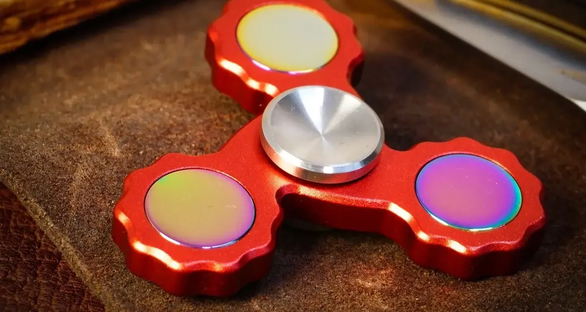 Röd fidget spinner med regnbågseffekter på de tre yttre delarna.