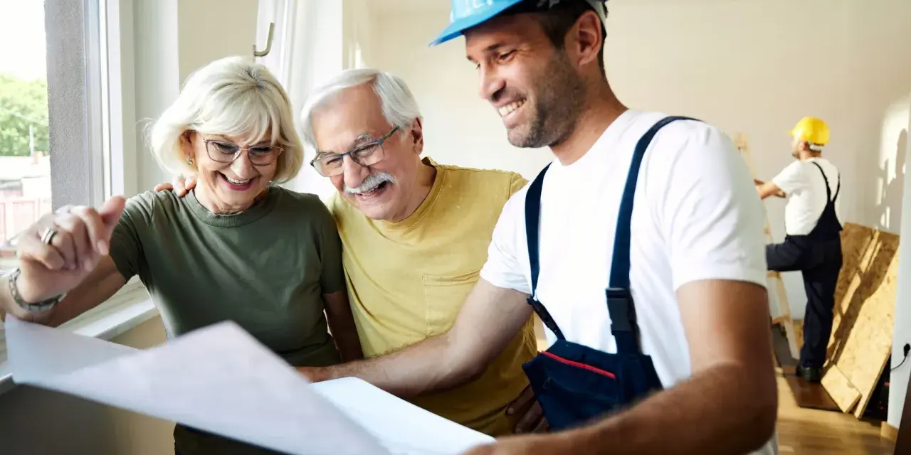 Pareja mayor sonríe mientras revisa planos con un constructor. Posibles bonificaciones mayores 65 años para su proyecto.