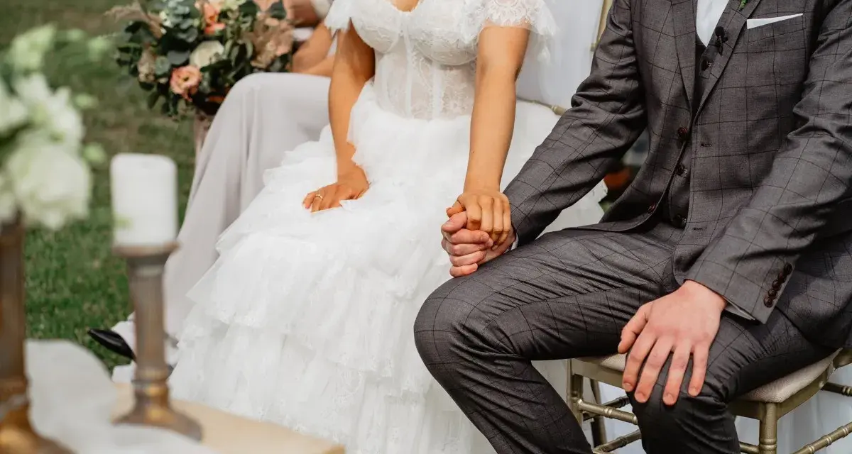 Para spowiedzi przedślubnej lub formalności w USC: panna młoda w koronkowej sukni i pan młody w garniturze trzymają się za ręce.