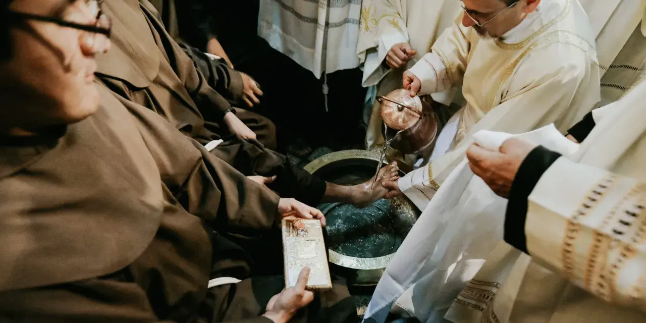 During a holy Thursday Catholic homily, a priest washes the feet of a man in a basin, symbolizing Christ's humility.
