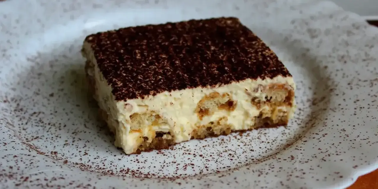 Pyszne tiramisu, czyli zabajone, na białym talerzu, posypane kakao.