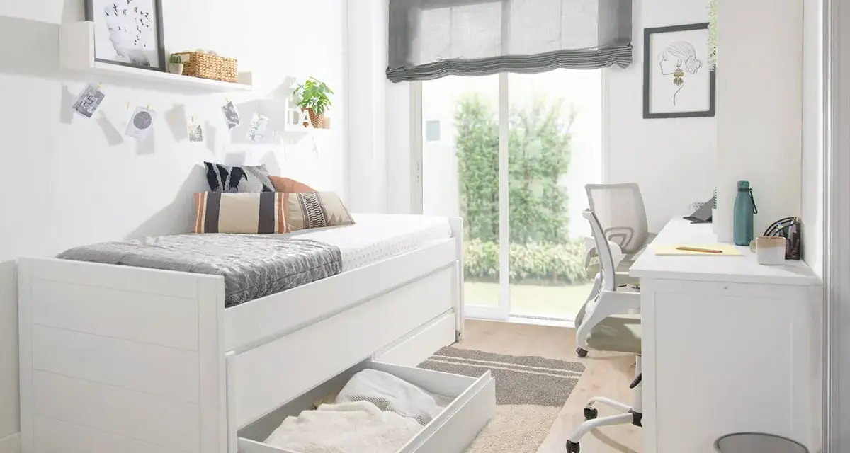 Habitación estrecha y alargada con cama blanca, escritorio y silla. Ventana grande con vistas al jardín.