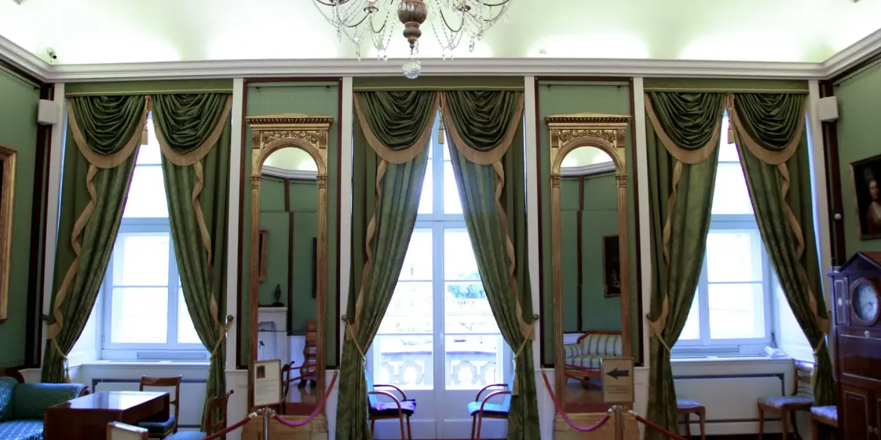 Wnętrze pałacu królewskiego we Wrocławiu. Eleganckie zielone zasłony, złote lustra i kryształowy żyrandol tworzą atmosferę dawnej świetności.