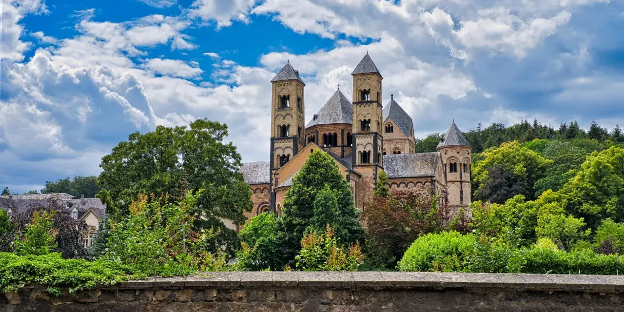 A grand Romanesque abbey, where Benedictine monks lived, stands amidst lush greenery under a dramatic sky.
