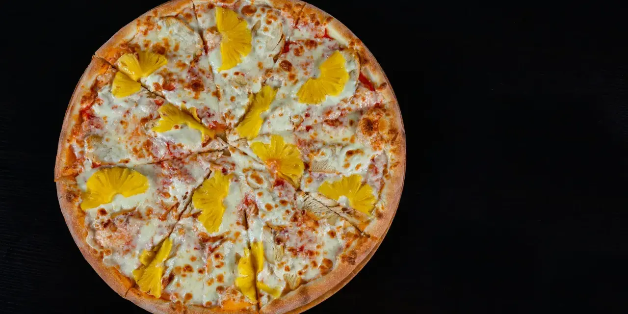 Pizza hawajska z kurczakiem i ananasem na czarnym tle.