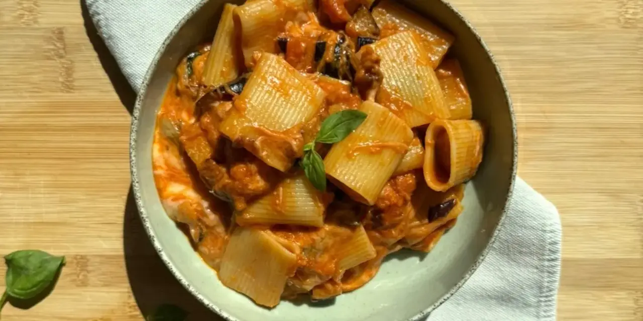 Piatto di pasta alla siciliana con rigatoni, melanzane e pomodoro, guarnito con basilico fresco.