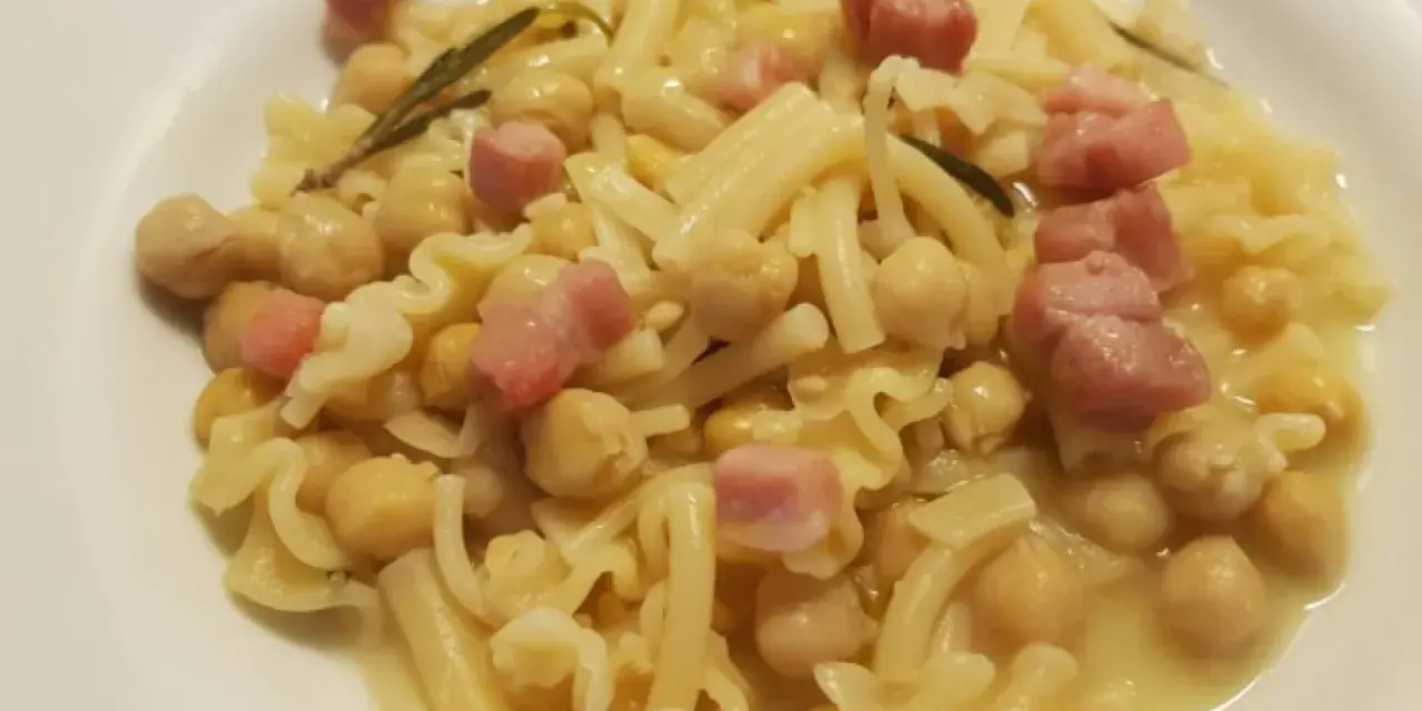 Piatto di pasta e ceci in scatola, con cubetti di pancetta e un rametto di rosmarino.