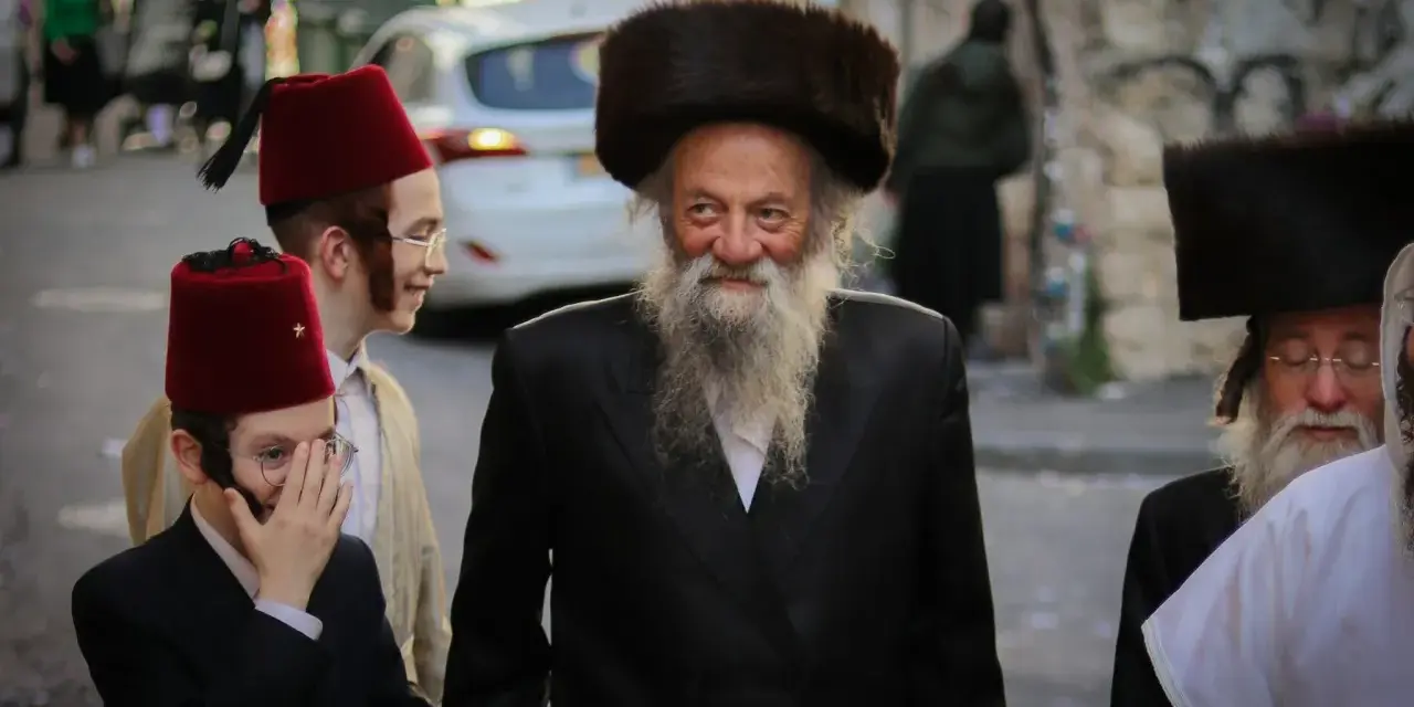 Men in traditional attire, including fur hats and red fez hats, walk together, perhaps celebrating the Purim meaning of joy and community.