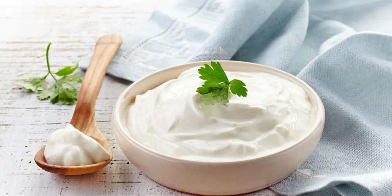 Gęsta, biała śmietana 30 kcal w miseczce, obok drewniana łyżka z porcją. Idealna do deserów i sosów.