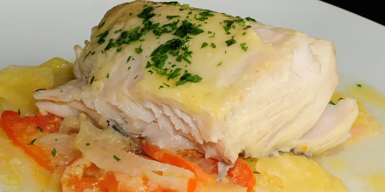 Cogote de merluza jugoso y tierno, servido sobre patatas y tomate, con un toque de perejil fresco.