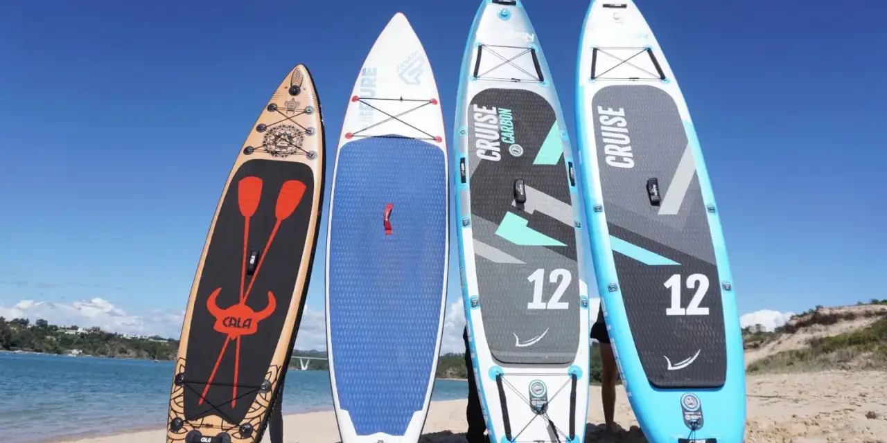 Vier Stand Up Paddles am Strand. Die Boards zeigen verschiedene Designs und Größen, die die Vor- und Nachteile von Stand up paddling beeinflussen können.