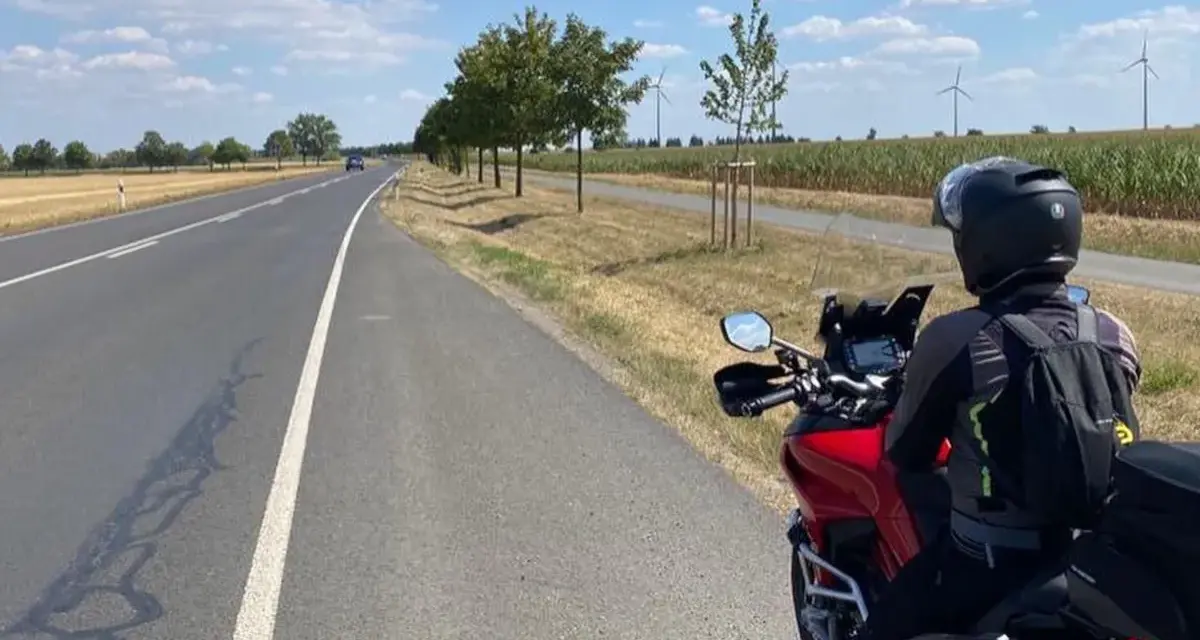 Motociclista su strada panoramica Foresta Nera, con campi di mais e pale eoliche all'orizzonte.