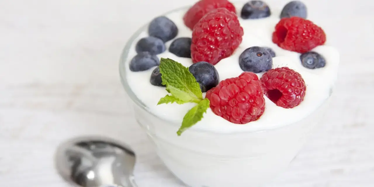 Pyszny jogurt z malinami i borówkami, idealny na śniadanie lub jako element diety jogurtowej. Obok leży łyżeczka.