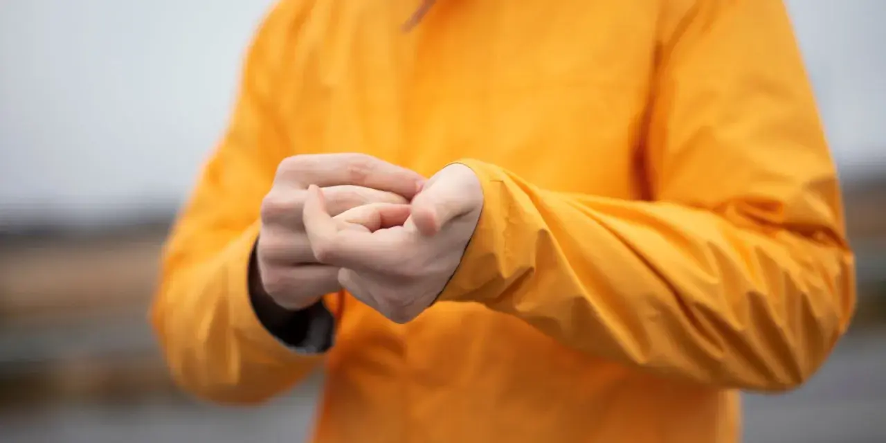 Persona se frota las manos dentro de una chaqueta naranja brillante. El poliéster da calor y protege del frío.