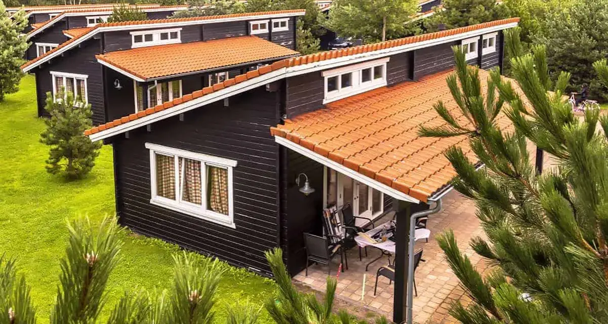 Czarny bungalow z pomarańczowym dachem, otoczony zielenią. To idealne miejsce na wypoczynek, co to znaczy bungalow?