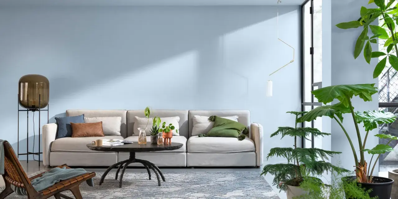 Jasny salon z wygodną kanapą, stolikiem kawowym i dużą ilością roślin. Sufit w kolorze ścian tworzy spójną, spokojną atmosferę.