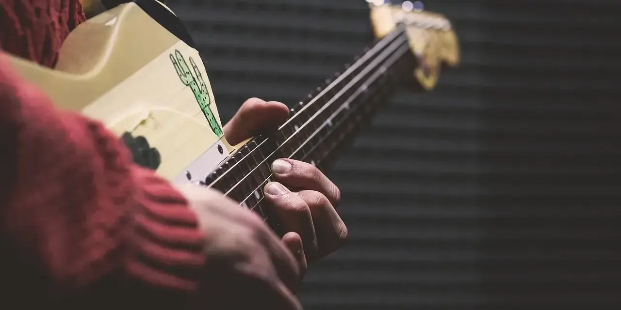 Dłonie grają na gitarze, ludowy instrument szarpany z rysunkiem kaktusa.