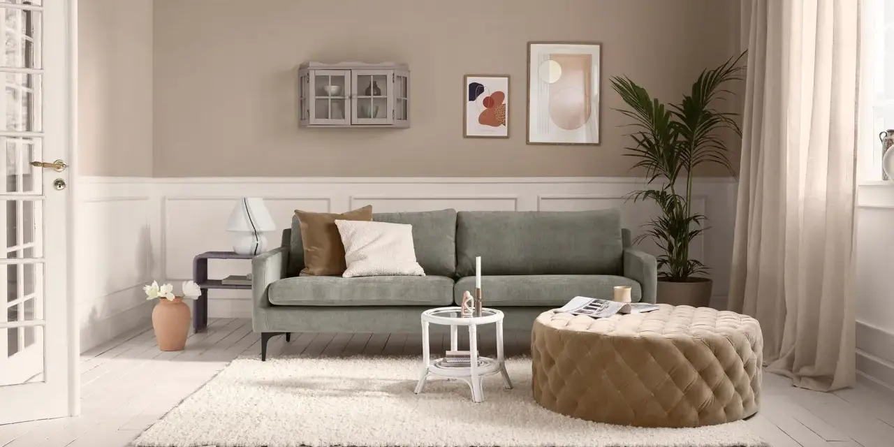 Gemütliches kleines Wohnzimmer einrichten mit grauem Sofa, beigem Hocker, weißem Teppich und Wanddeko.