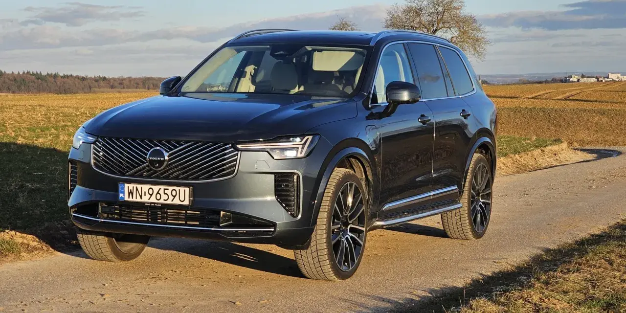 Ciemnoszary Volvo XC90 T8 na tle jesiennego krajobrazu. Elegancki SUV z nowoczesnym grillem i światłami LED.