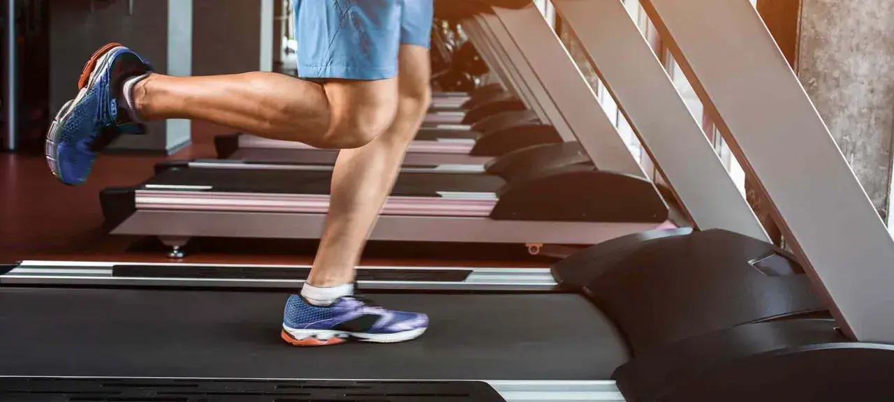 Gambe muscolose in movimento su un tapis roulant, simbolo di corsa indoor e allenamento.
